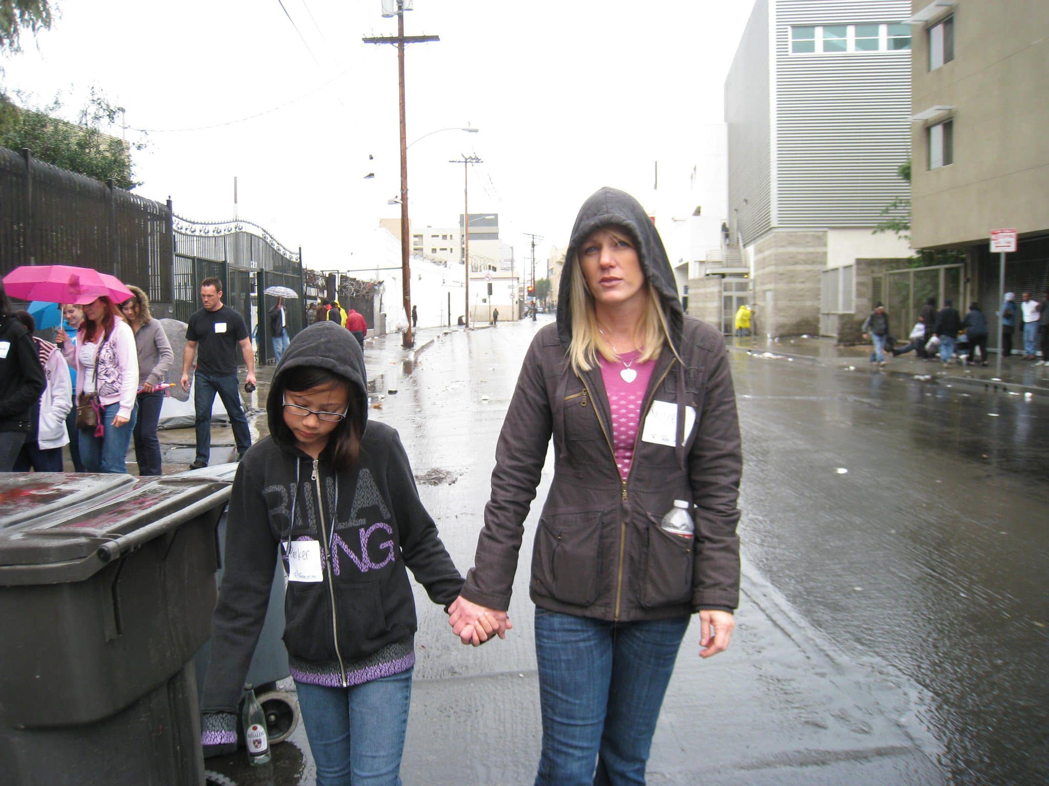 Michelle holding a child's hand while walking with volunteers on a rainy Skid Row street in Los Angeles